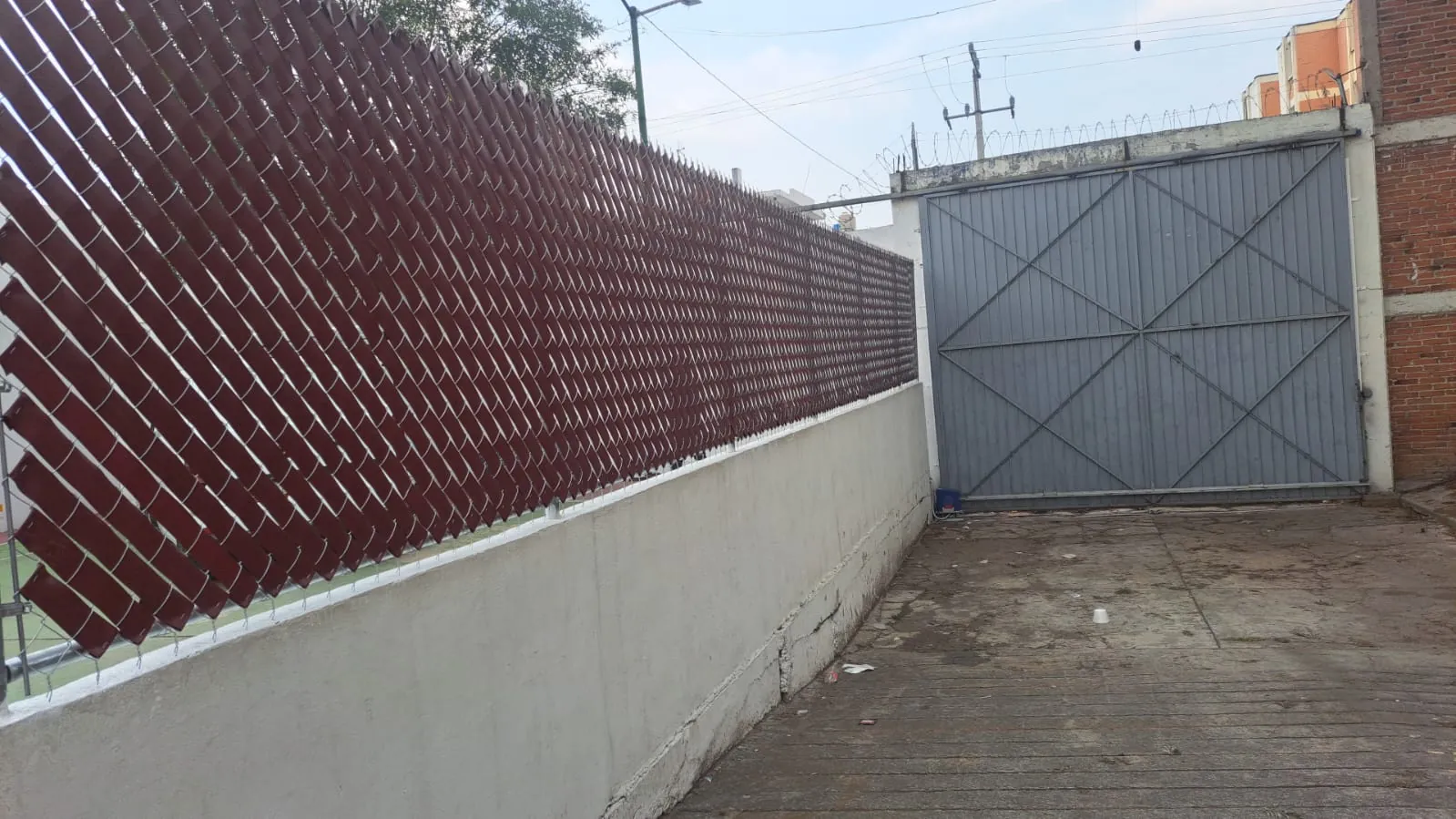 Cinta de privacidad guinda en malla ciclónica junto a un portón metálico con concertina