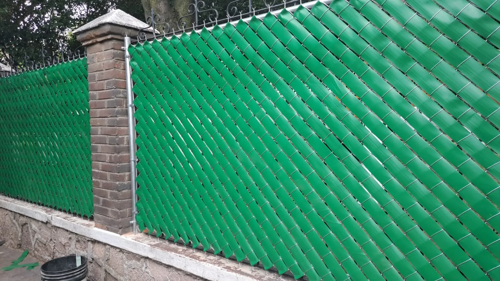 Cinta de privacidad verde tejida en malla ciclónica sobre una barda de ladrillo