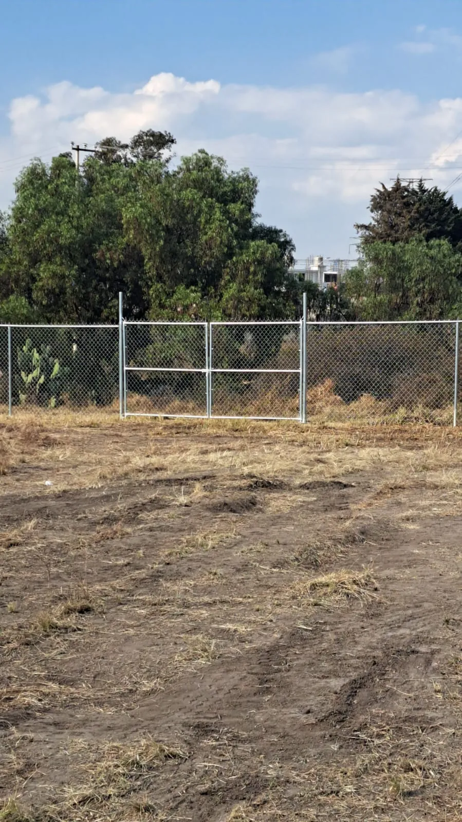 Portón de malla ciclónica galvanizada instalado en un terreno cercado